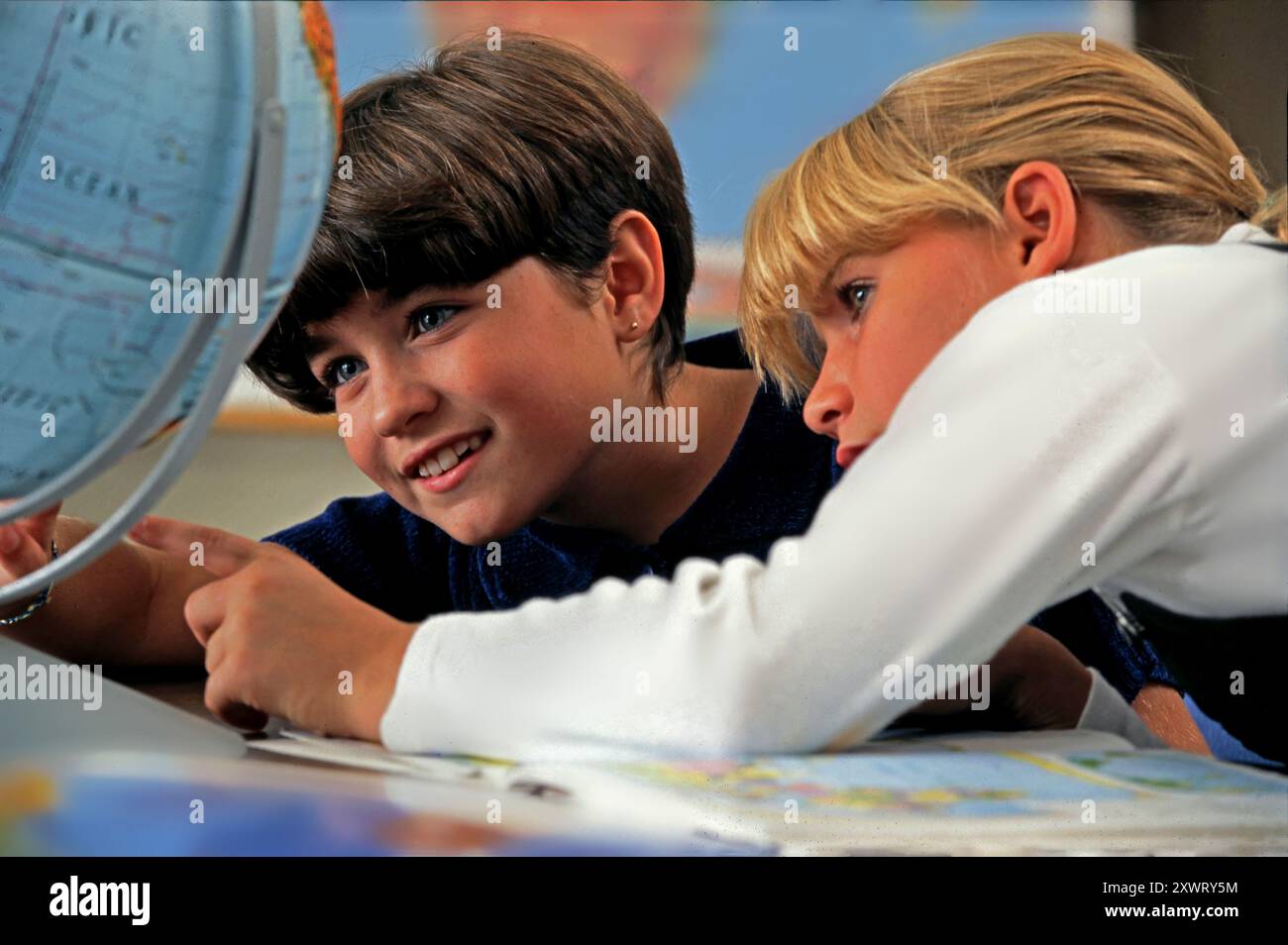 Due giovani studentesse esaminano un globo mentre studiano le mappe, discutono con entusiasmo della geografia e imparano insieme nella loro classe. Foto Stock