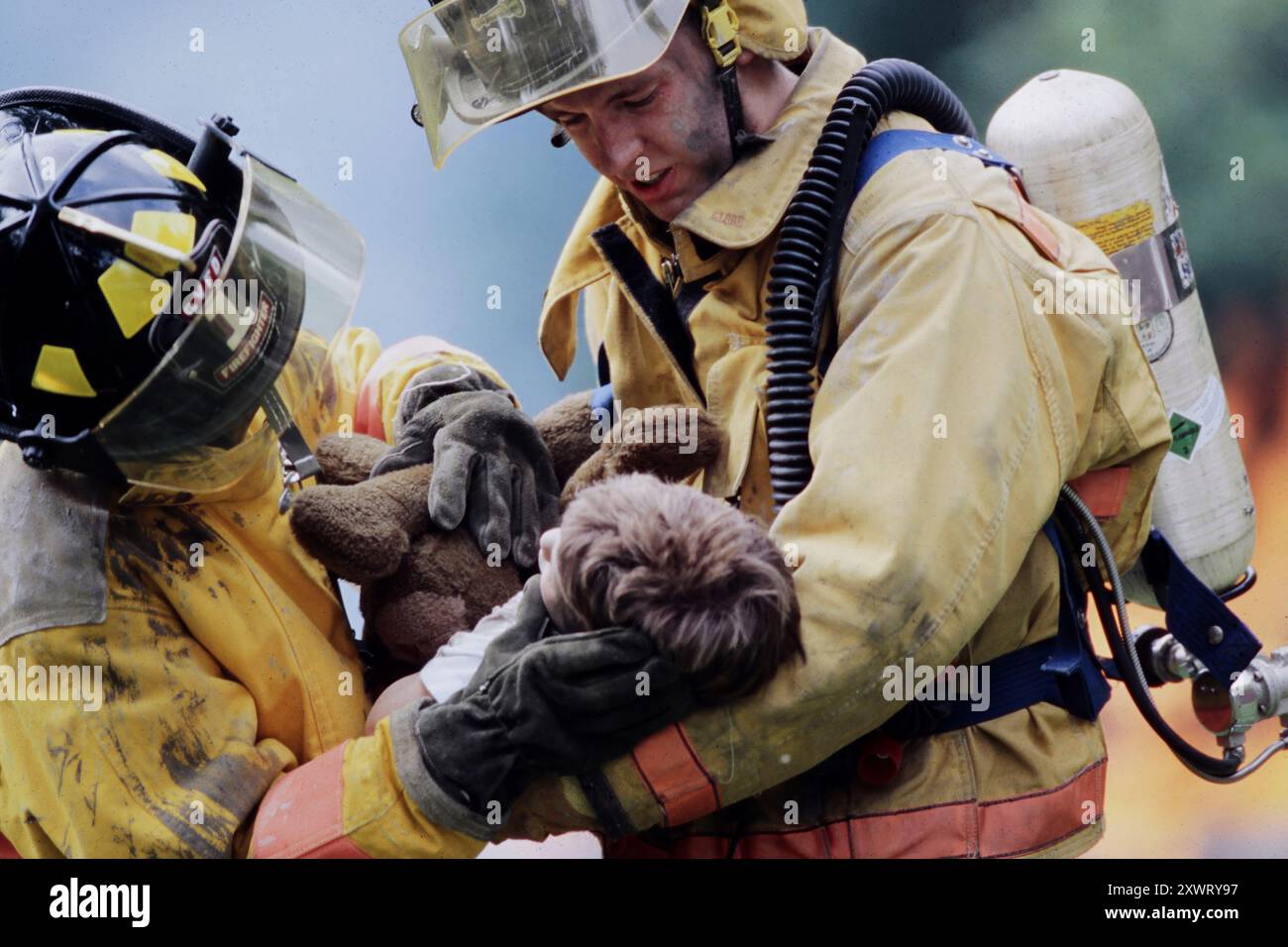 Due vigili del fuoco portano un bambino e un orsacchiotto lontano da un incendio, dimostrando coraggio e compassione in un momento critico. Foto Stock