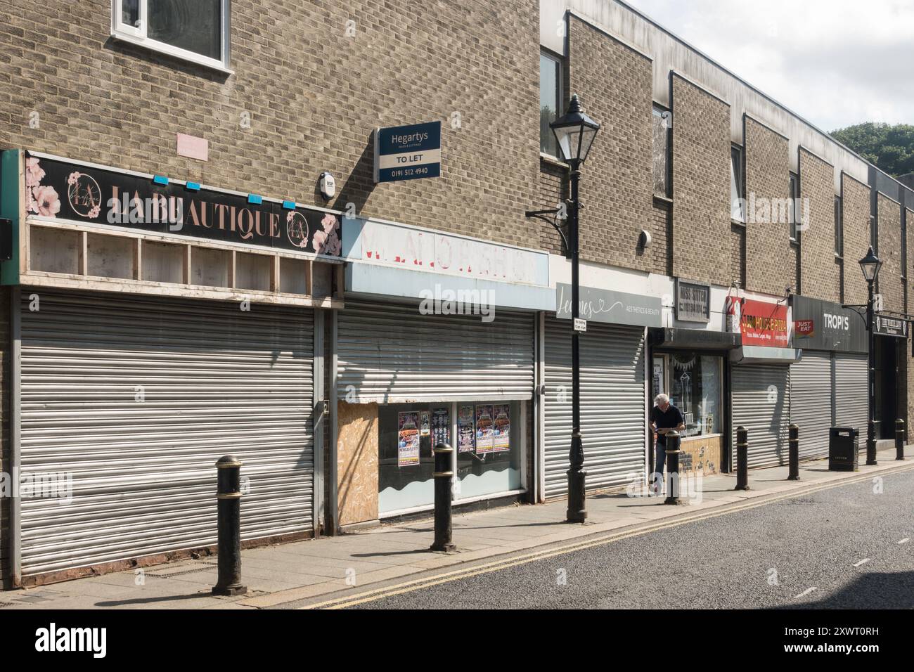 Un uomo cammina accanto ai negozi a bordo nel centro di Houghton le Spring, Tyne and Wear, Inghilterra, Regno Unito Foto Stock