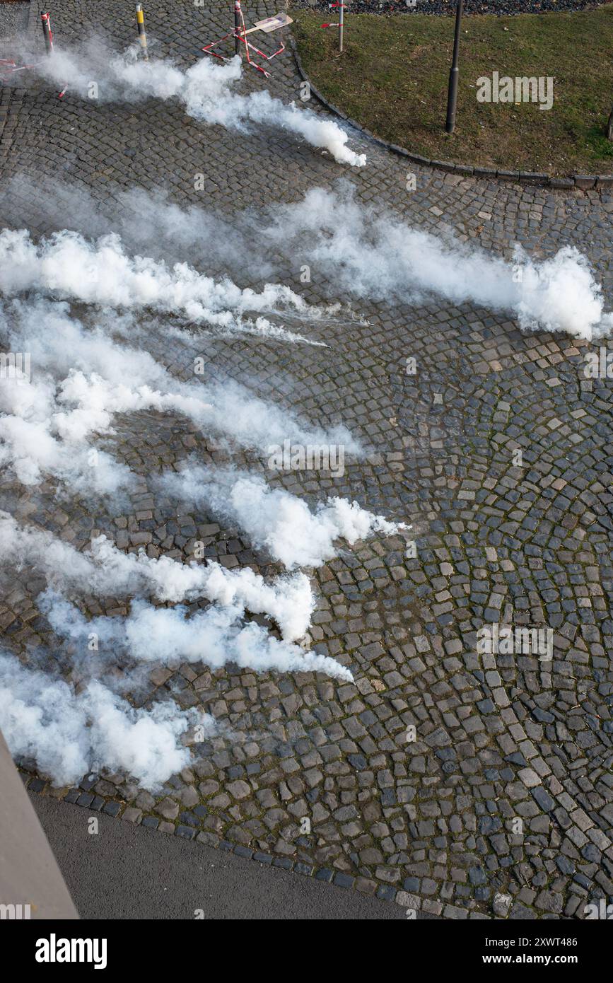 Vista aerea delle bombole di gas lacrimogeni che creano spesse nuvole di fumo su una strada acciottolata, utilizzate come misura di controllo della folla durante una protesta. L'immagine trasmette caos, tensione e disordini civili. Foto Stock