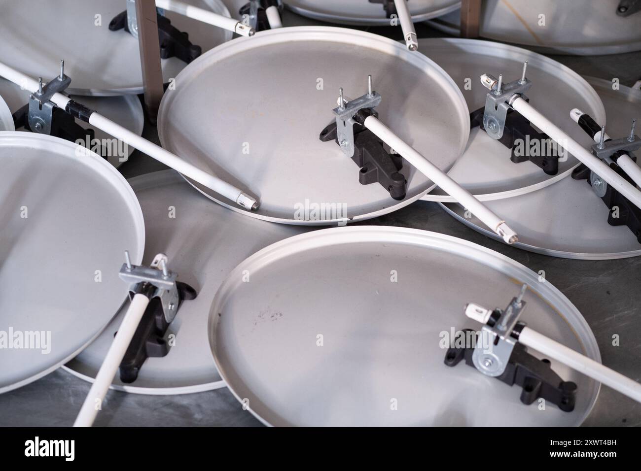 Primo piano dettagliato delle parti smontate delle parabole satellitari organizzate in un'officina. L'immagine simboleggia la cooperazione e l'assemblaggio complesso. Perfetto per temi tecnologici, ingegneristici e di telecomunicazione. Foto Stock