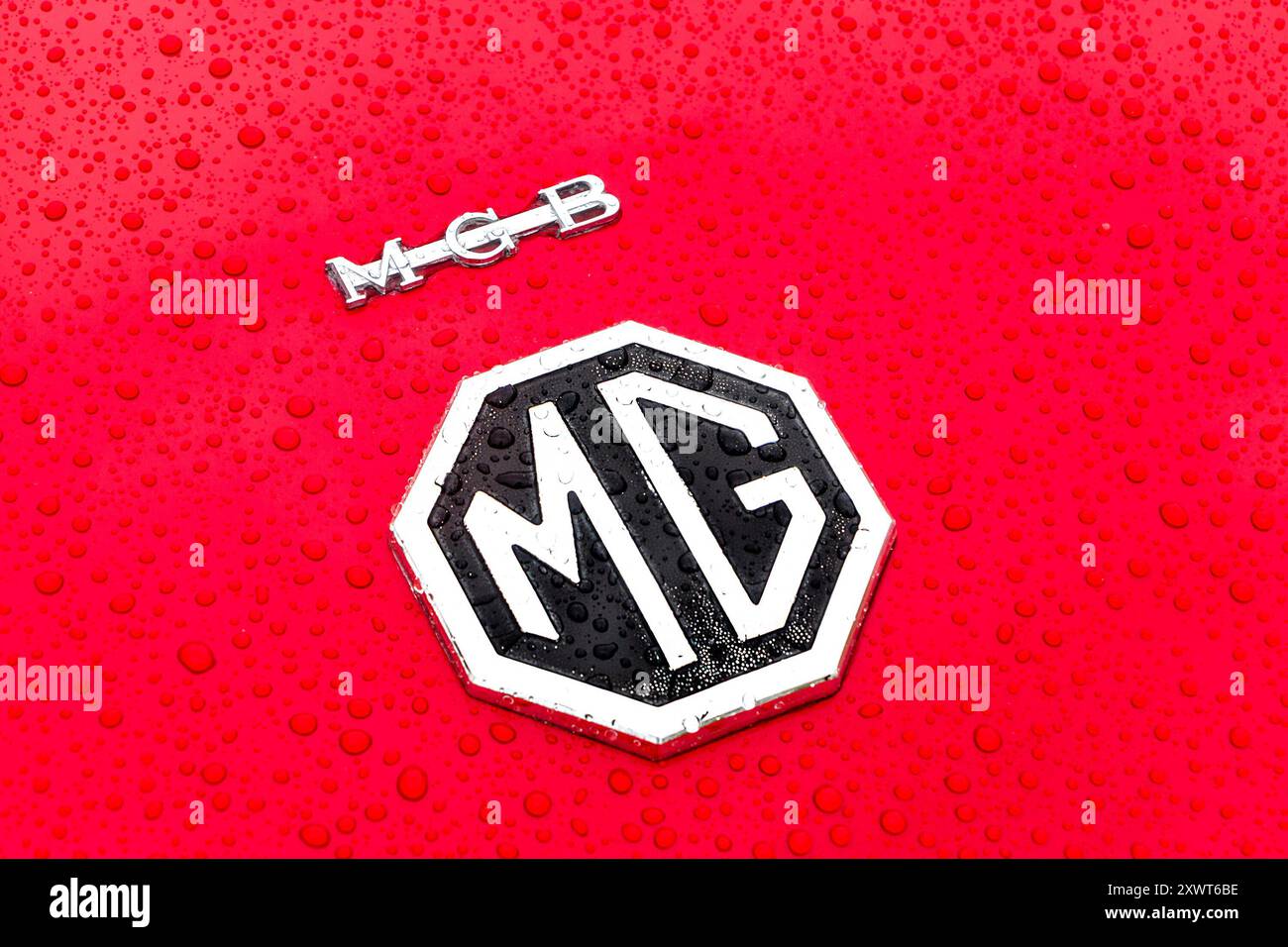 Primo piano del logo MG su un'auto rossa con gocce d'acqua sulla superficie. MGB Foto Stock