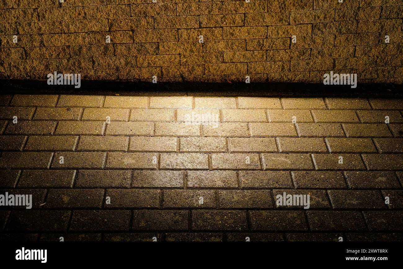 Pavimento pavimentato illuminato da luce stradale: Motivo e consistenza - luce e ombra. Bagliore dorato. Foto Stock