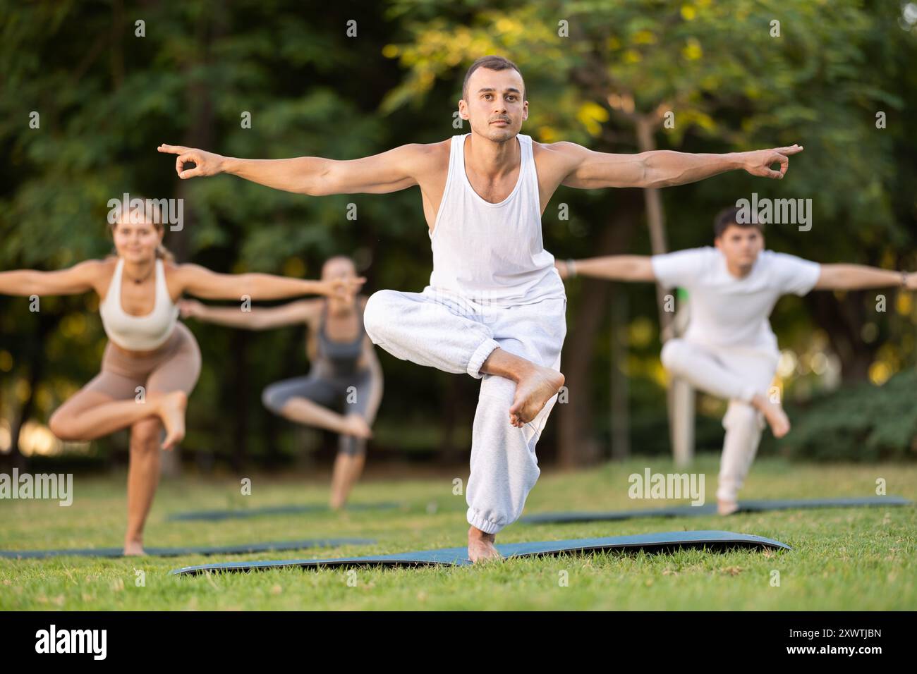 Uomo che esegue Eka Pada Utkatasana durante la lezione di yoga di gruppo nel parco Foto Stock
