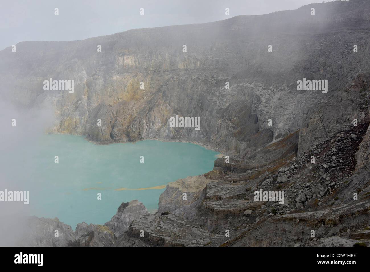 Eingekreist von einer zerfurchten Felswand liegt im Krater des Gunung Iljen der Kratersee. Seine grünlich-blaue Farbe ist auf hohe Konzentrationen von Alaun, Schwefel und GIPS zurückzuführen. MIT einem pH-Wert um 0,3 und Seiner wird als größtes Säurefass der Erde bezeichnet. Kratersee - Breite: 600 m - Länge: 960 m - Tiefe: bis zu 200 m *** circondato da una parete rocciosa solcata, il lago cratere si trova nel cratere di Gunung Iljen il suo colore blu verdastro è dovuto alle alte concentrazioni di alluminio, zolfo e gesso con un valore di pH di circa 0,3, è noto come il più grande barile di acido sulla terra Crate Foto Stock