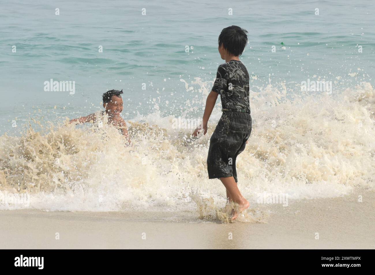 Zwei Jungs haben am White Sand Beach Pantai Bias Tugel Spaß mit den Wellen. *** Due ragazzi si divertono con le onde a White Sand Beach Pantai Bias Tugel Foto Stock