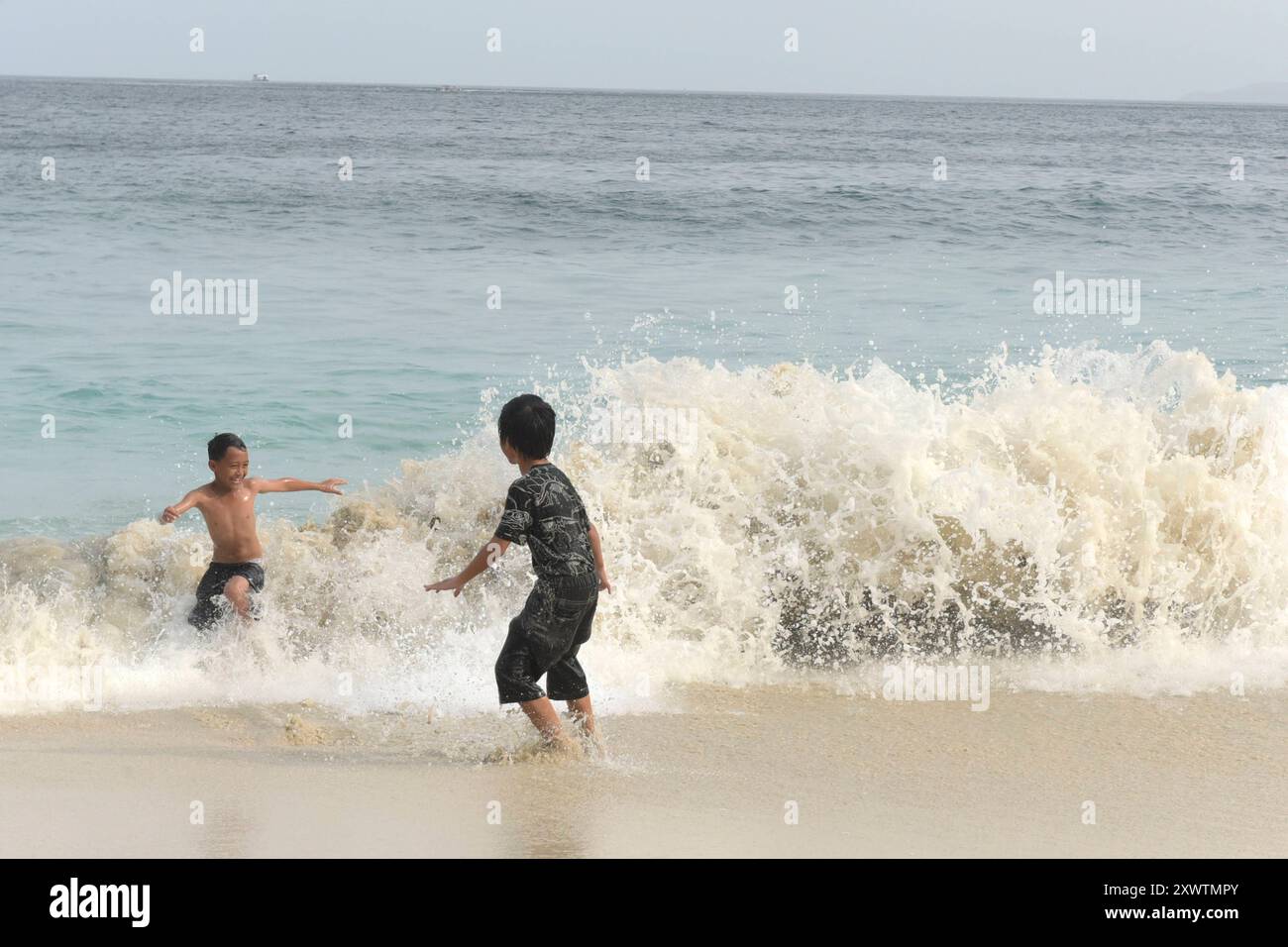 Zwei Jungs haben am White Sand Beach Pantai Bias Tugel Spaß mit den Wellen. *** Due ragazzi si divertono con le onde a White Sand Beach Pantai Bias Tugel Foto Stock