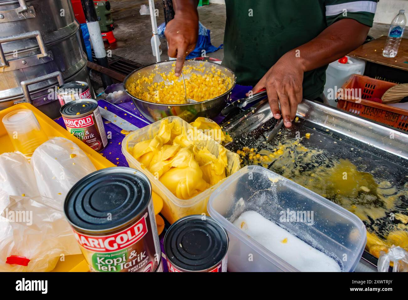 Un venditore mescola il burro con il mais dolce cotto in una ciotola pronta per essere venduta come spuntino ai clienti in una bancarella di mercato a Tanjung Bunghah, Penang, Malesia Foto Stock