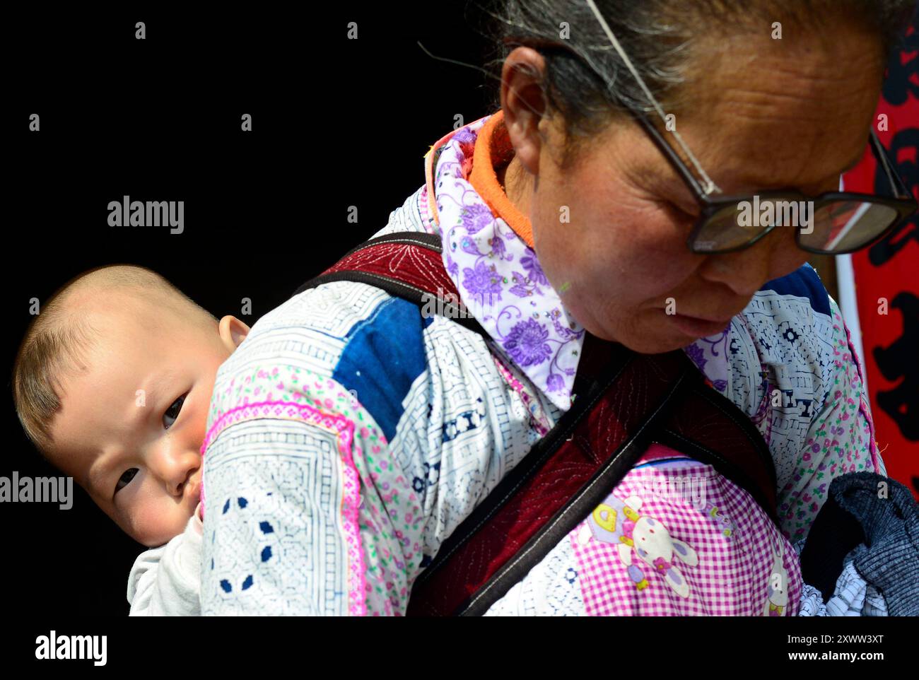 Una lunga Miao a corno che porta il nipote sulla schiena. Guizhou, Cina. Foto Stock