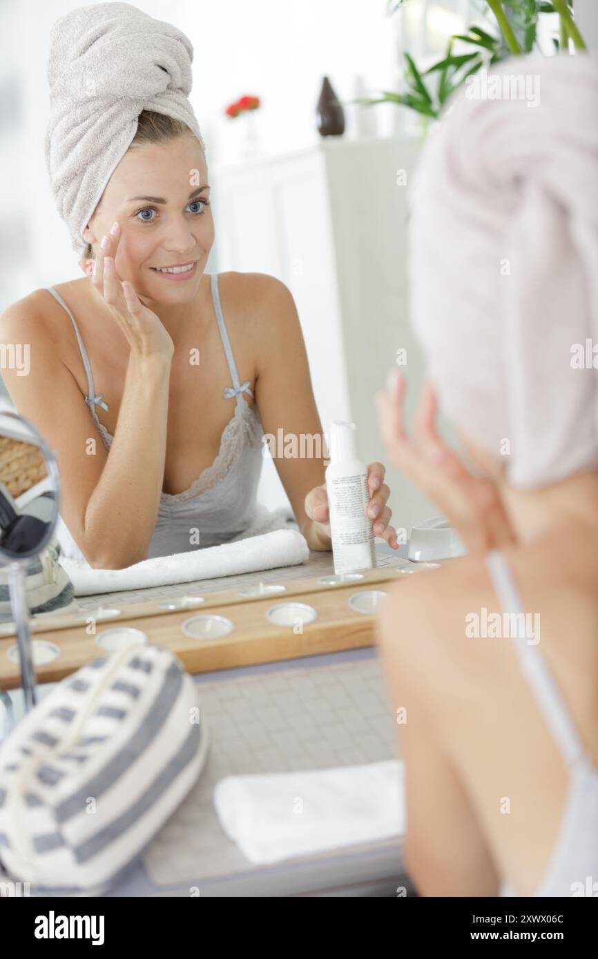 donna che guarda allo specchio che applica prodotti di bellezza intorno agli occhi Foto Stock