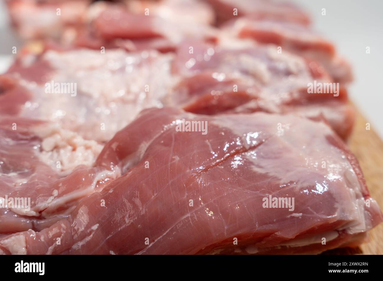 Una lastra di carne viene visualizzata su un tagliere di legno. La carne è cruda e ha un aspetto lucido e umido Foto Stock