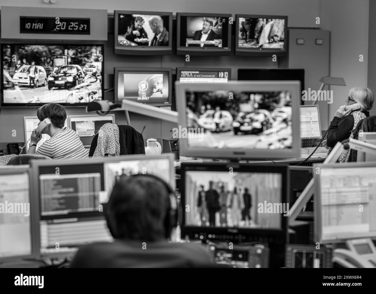Immagine in bianco e nero che raffigura una vivace sala stampa ad Amburgo. I giornalisti si vedono lavorare sui computer e discutere al telefono. Più schermi visualizzano vari contenuti di notizie, catturando l'essenza di un'impostazione multimediale dinamica. Foto Stock