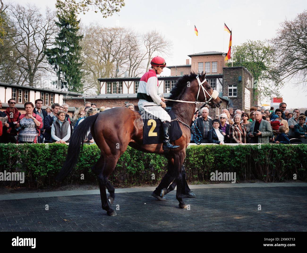 Jockey Andreas Suborics e il cavallo da corsa OVERDOSE nel paddock dell'ippodromo Hoppegarten di Berlino durante l'apertura della stagione il 17 aprile 2011. La scena cattura l'attesa e l'energia di un evento ippico, con gli spettatori impazienti di guardare. Foto Stock