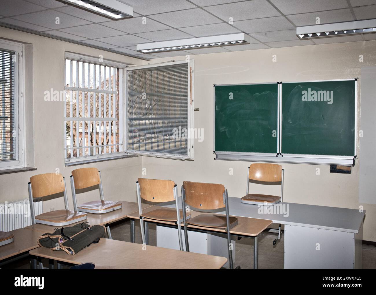 Un'aula all'interno della prigione Tegel di Berlino, Reinickendorf, con scrivanie vuote, sedie e una lavagna. Le finestre barrate sottolineano la giustapposizione di istruzione e confinamento, evidenziando metaforicamente i vincoli e le possibilità all'interno degli ambienti di apprendimento. Foto Stock
