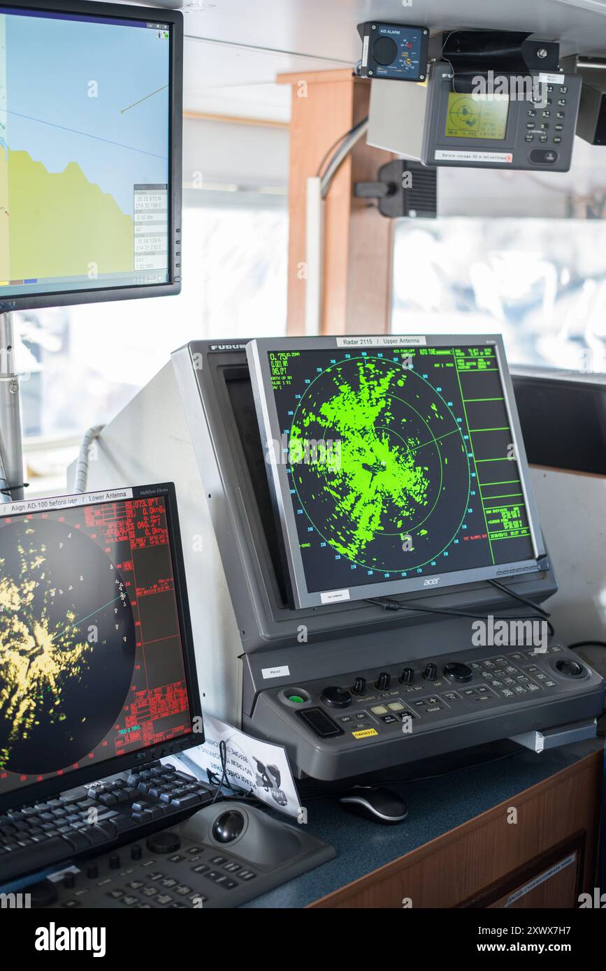 Una visione dettagliata di un moderno sistema di navigazione navale dotato di più schermi radar e di apparecchiature di monitoraggio avanzate. Ideale per illustrare la tecnologia marittima, la navigazione e i sistemi di comunicazione utilizzati nelle operazioni navali. Foto Stock