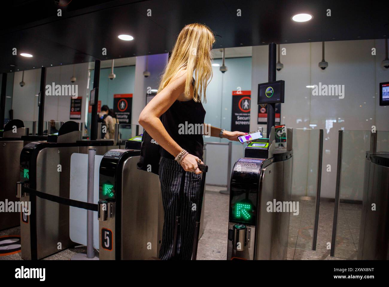 Un passeggero passa attraverso i cancelli di sicurezza del Terminal 3 dell'aeroporto di Heathrow. Questo porta alla sala partenze. Foto Stock