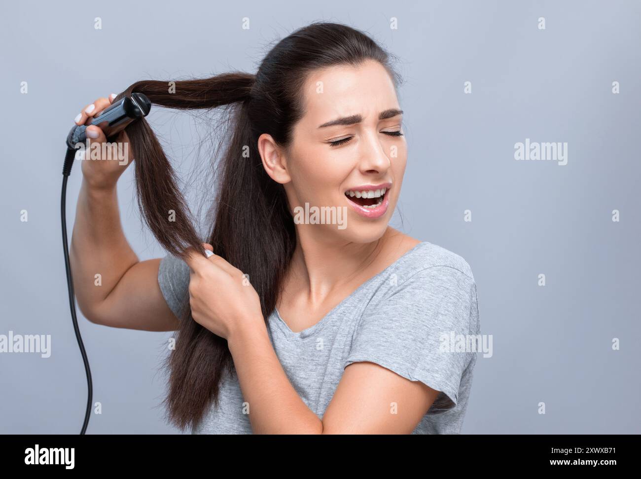 La giovane donna fa lisciare i capelli ricci. Ritratto di una bella ragazza con lunghi capelli scuri, pelle pulita. Si arriccia durante la procedura. Il concetto di h Foto Stock