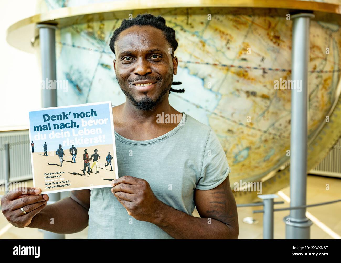 Schleswig, Germania. 20 agosto 2024. Il nigeriano Steven Ken Ojo presenta la sua brochure "Think Again before you risk your Life" davanti al Gottorf Globe. Ken Ojo è venuto in Europa illegalmente anni fa ed è stato ripetutamente esposto a un grande pericolo. Ora vuole educare le persone del suo paese su quanto sia pericoloso lasciare impreparato il suo paese d'origine con l'obiettivo di forzare la sua strada verso l'Europa. Credito: Axel Heimken/dpa/Alamy Live News Foto Stock