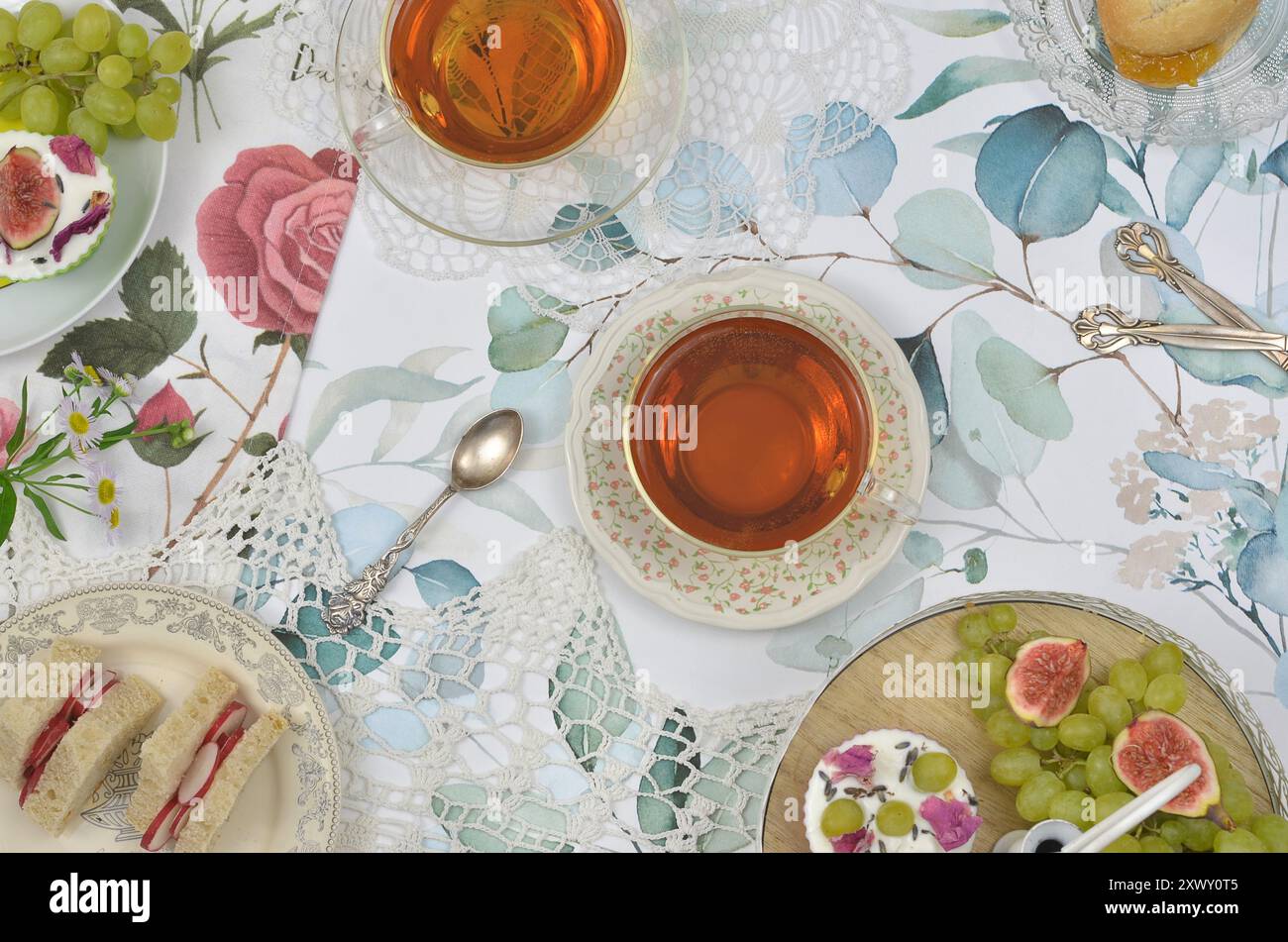 Festa del tè vintage in stile britannico: Due tazze di tè, frutta, tè panini triangolari, scone con marmellata e cupcake sull'altopiano. Vista dall'alto. Foto Stock