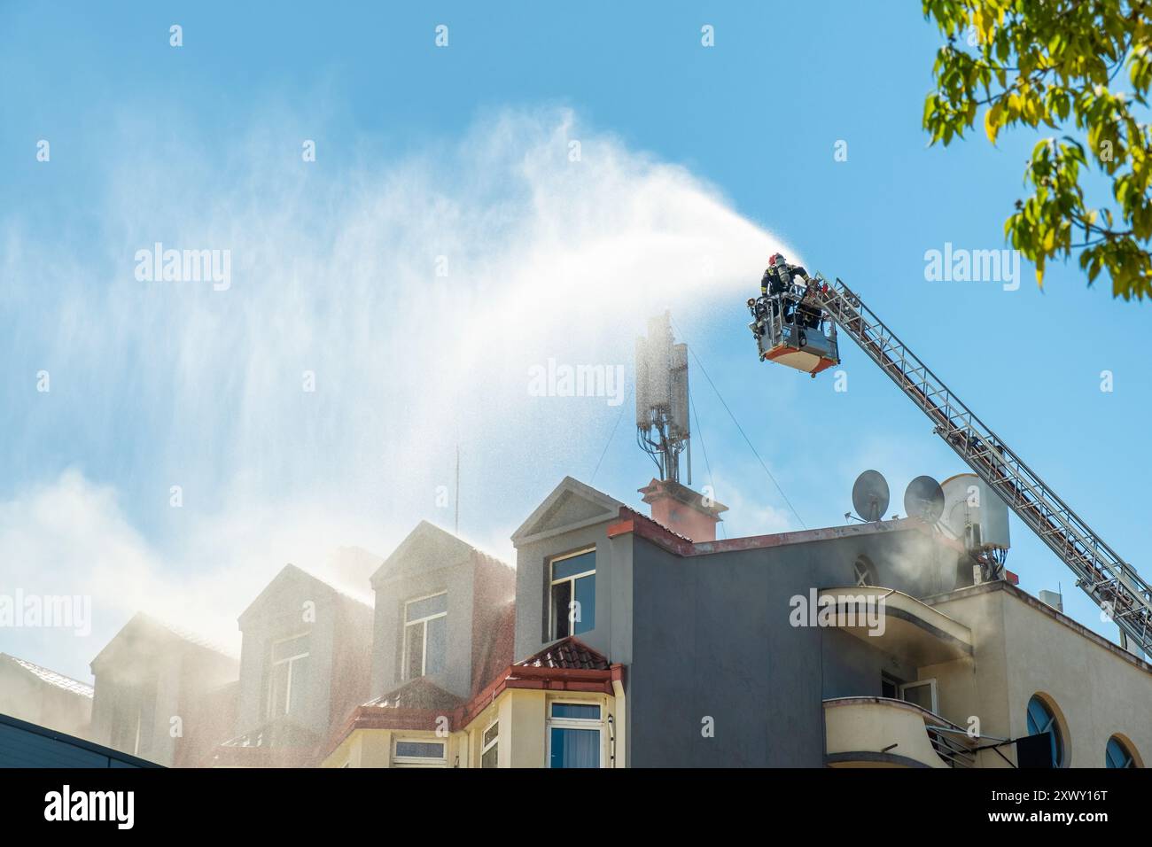 I vigili del fuoco estinguono la casa in fiamme utilizzando una scala estesa dotata di tubo flessibile per spruzzare acqua sul tetto dell'edificio con fumo. Pompiere Foto Stock