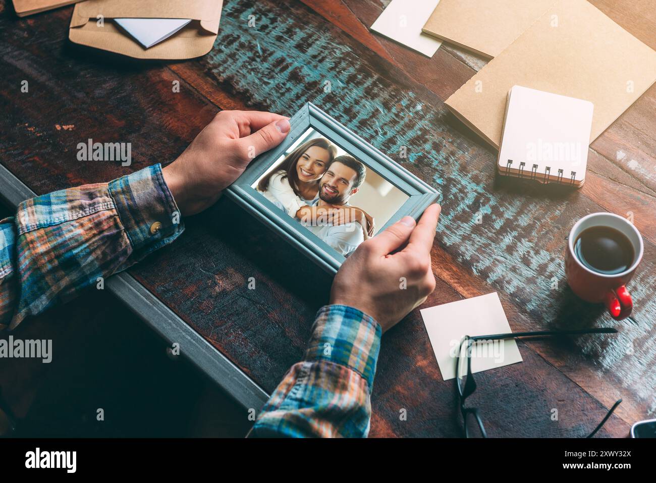 Bei ricordi. Immagine ravvicinata dall'alto di un uomo che tiene la cornice mentre è seduto al rustico tavolo di legno Foto Stock