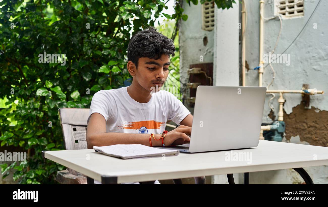 Gli studenti indiani del villaggio imparano online con il computer portatile e fanno i compiti all'aperto. Foto Stock