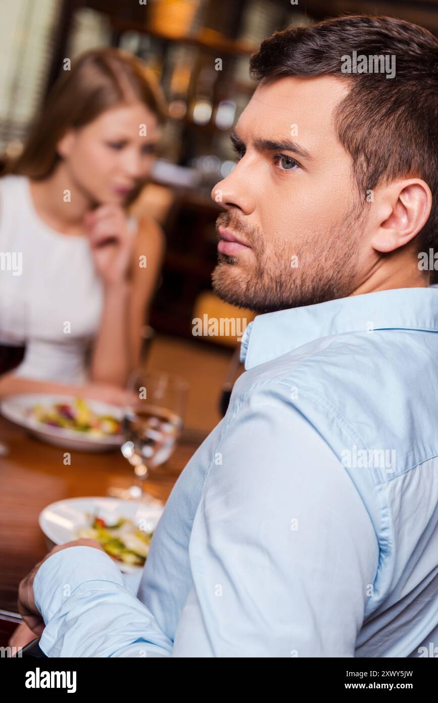 Difficoltà di relazione. Un giovane frustrato che guarda lontano mentre si siede insieme alla sua ragazza al ristorante Foto Stock