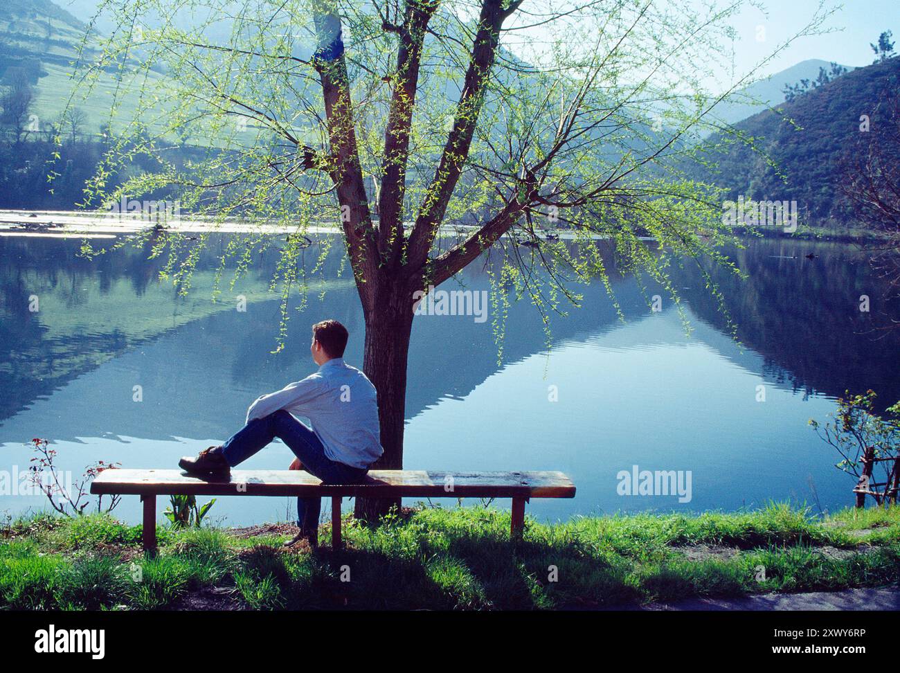 Uomo seduto sulla panchina, a guardare il lago. Cangas del Narcea, Asturie, Spagna. Foto Stock