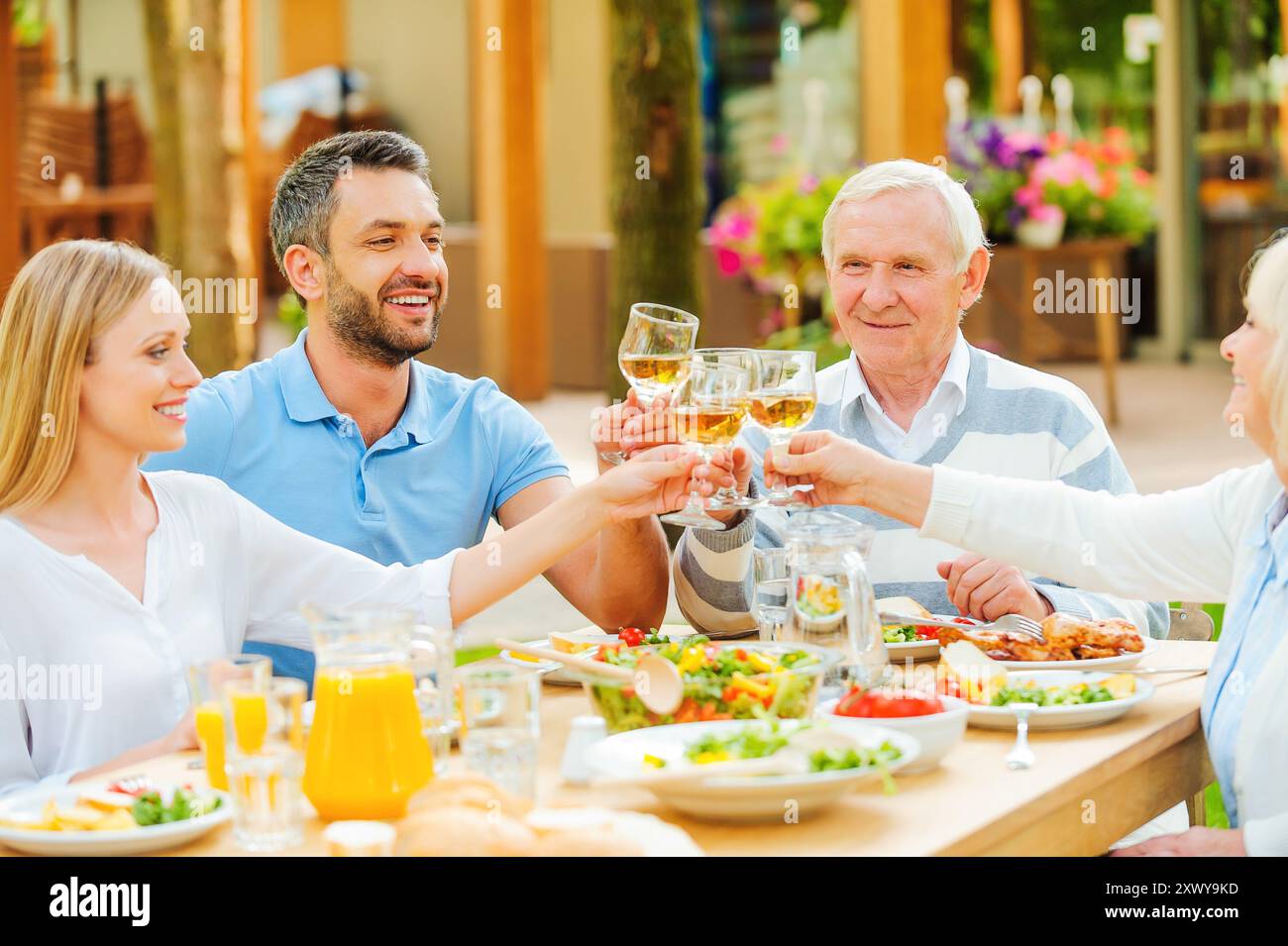 Saluti al più vicino! Coppie giovani e anziane felici sedute al tavolo da pranzo e brindate con vino Foto Stock