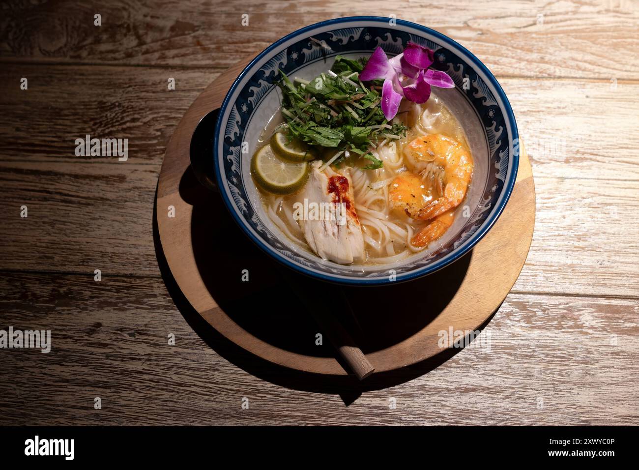 Zuppa di gamberi di pollo pho spaghetti in una ciotola con lime e fiori di orchidea hawaiana viola Foto Stock