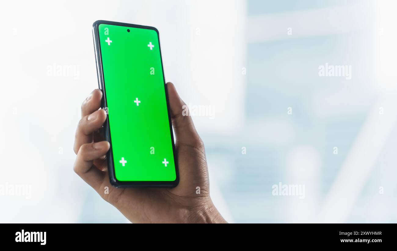 Persona aziendale anonima che utilizza uno smartphone con schermo di mascheratura verde per la pubblicazione sui social media. Mano dell'uomo che tiene il cellulare in verticale con area isolata per app, software, promozione sito Web Foto Stock