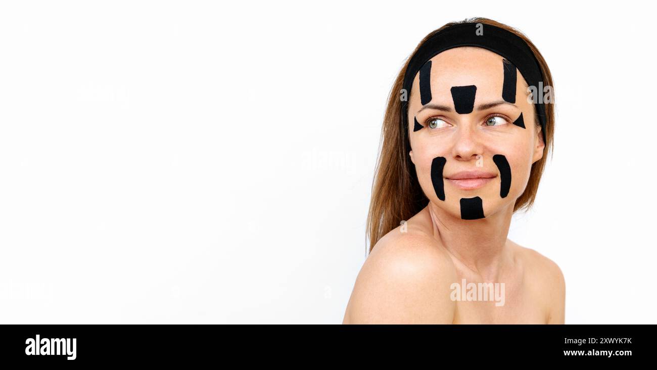 Giovane modella di bellezza con nastri facciali neri sul viso davanti a sfondo bianco. Foto Stock