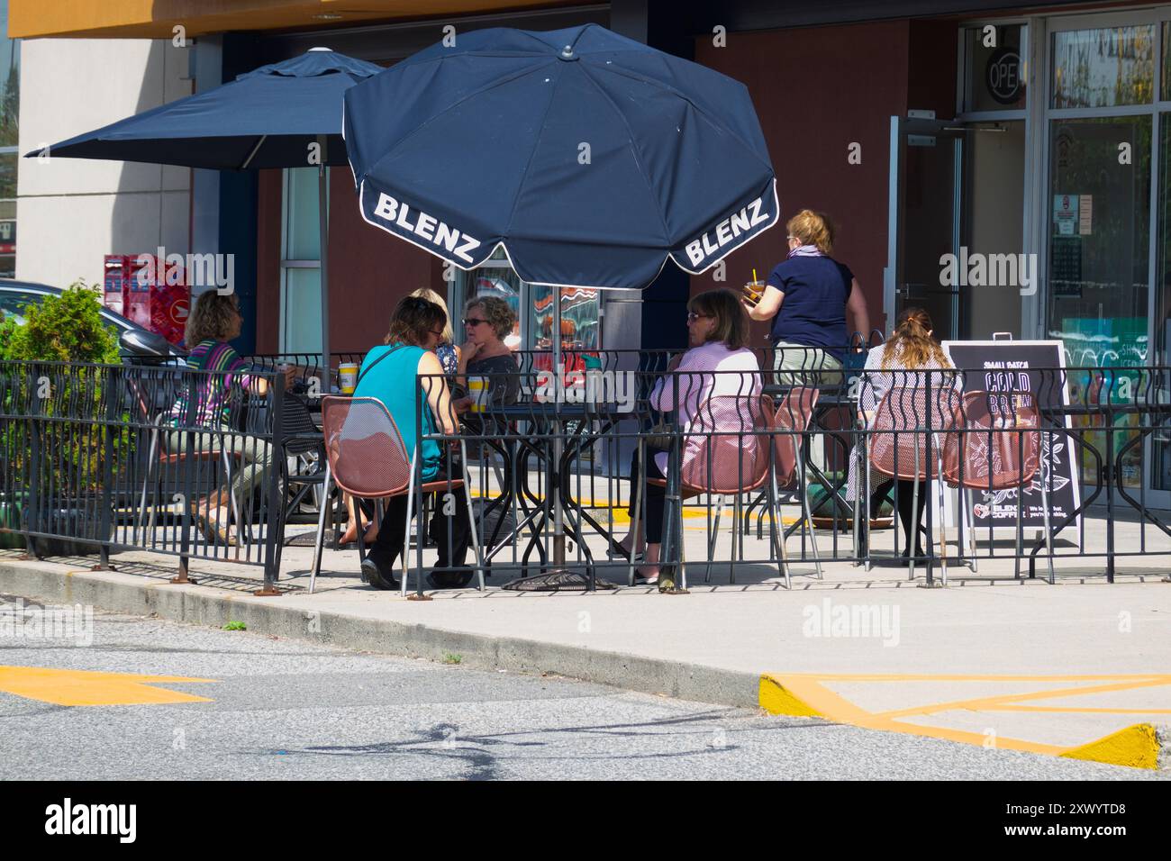 Donne sedute a bere un caffè e chiacchierare sotto un ombrello del patio alla caffetteria Blenz nel centro di Maple Ridge, B. C., Canada. Foto Stock