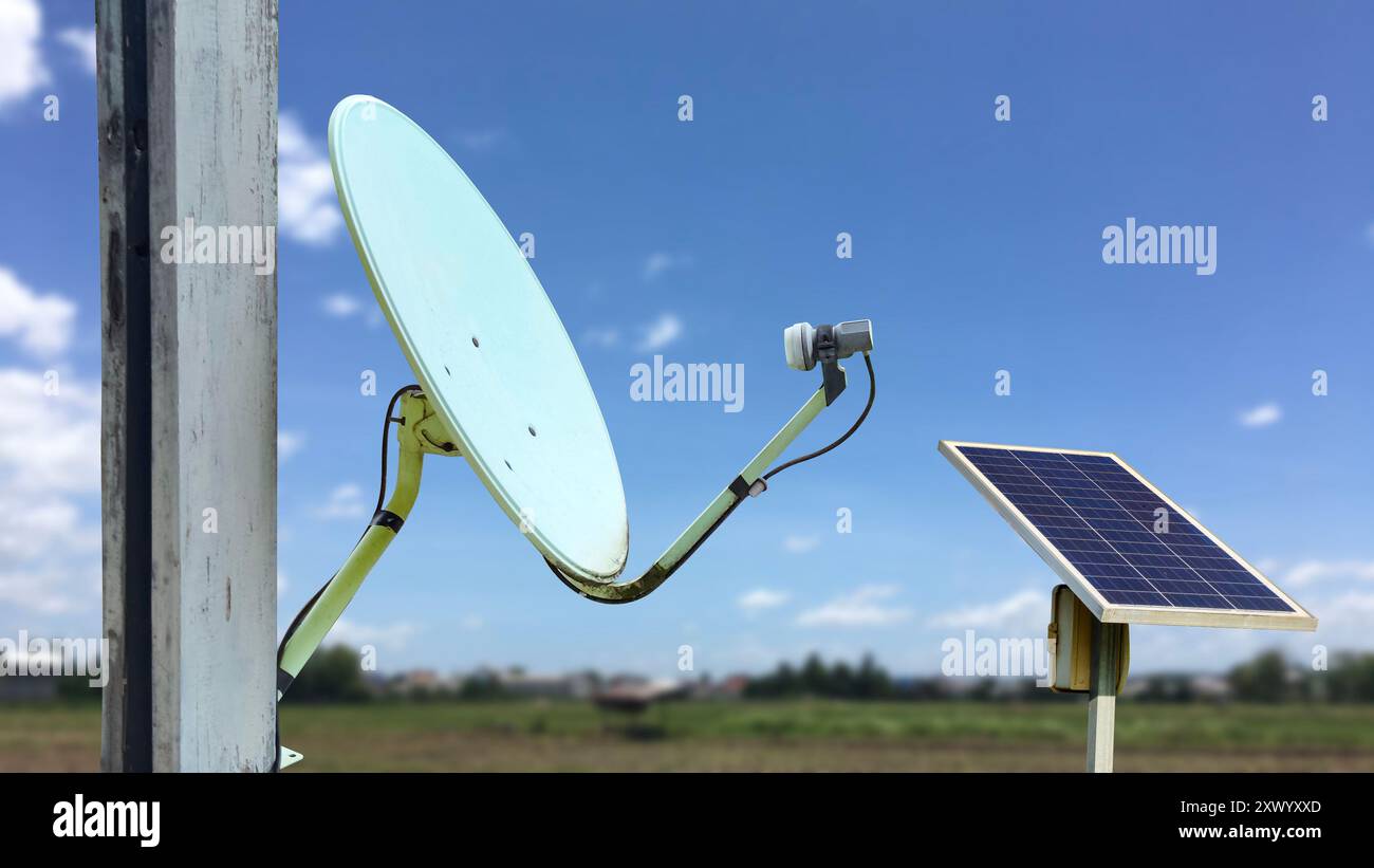 Immagine di una vecchia parabola satellitare montata su un palo, abbinata a un pannello solare per ottenere energia, consentendo la comunicazione e la ricezione di notizie in remoto A. Foto Stock