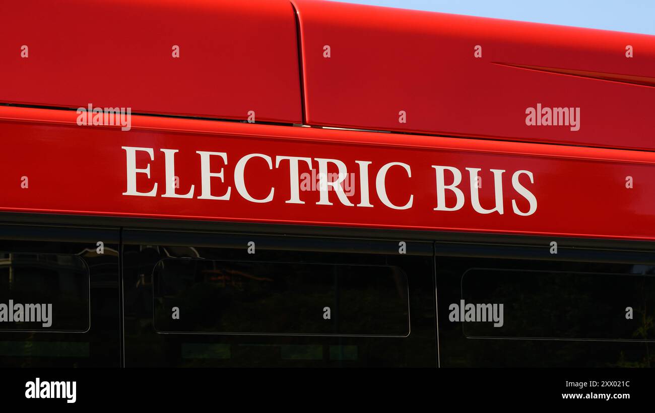 Bus elettrico con testo bianco sul lato dell'autobus rosso in primo piano Foto Stock