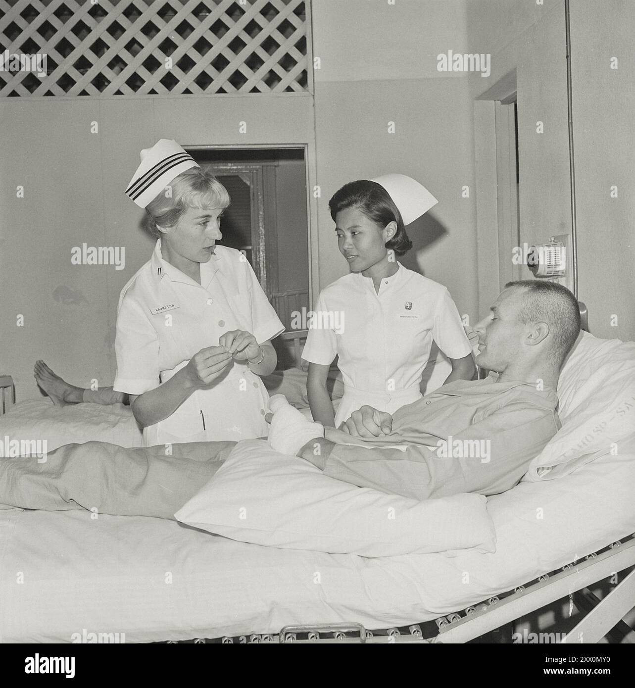 Guerra del Vietnam. Il tenente Frances Crumpton e la signorina Nangnoi Tongkim, un'infermiera thailandese, parlano con un soldato americano ferito nella guerra del Vietnam. Gli infermieri lavorano nell'ospedale della Marina di Saigon. Saigon, Vietnam del Sud. Febbraio 1966 Foto Stock