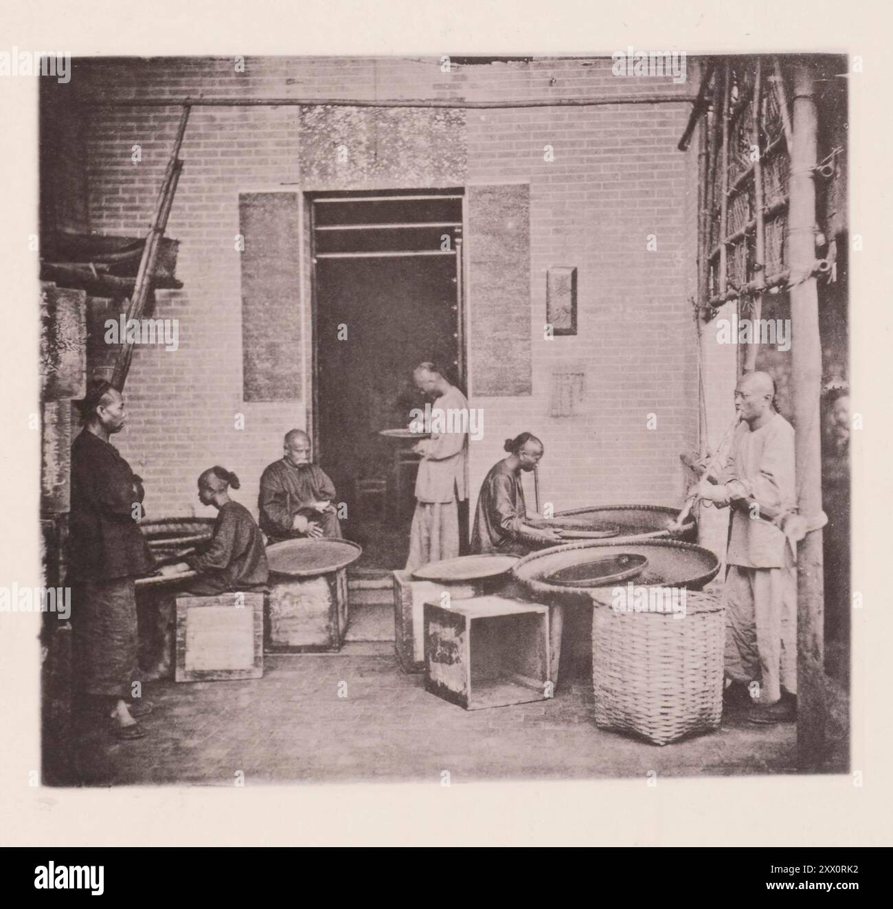 Foto d'epoca della produzione di tè a Canton (Guangzhou). Una casa da tè. Illustrazioni di Qing Cina, 1875 ... gli stabilimenti di cottura del tè autoctoni di Canton sono adiacenti al fiume, o alle rive di un torrente, e un molo di granito o legno è uno dei loro accessori più indispensabili. Durante la stagione del tè si possono osservare diversi uomini nella parte anteriore della casa, impiegati, come mostrato nella fotografia, nella raccolta, nel campionamento e nella cernita del tè o nella preparazione dei cassetti per la sua ricezione. Foto Stock