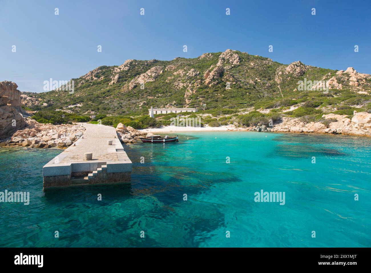 Ammira le limpide acque turchesi fino alla fine sabbia bianca della Spiaggia di Punta Rossa Corsara, molo in primo piano, Sardegna Foto Stock