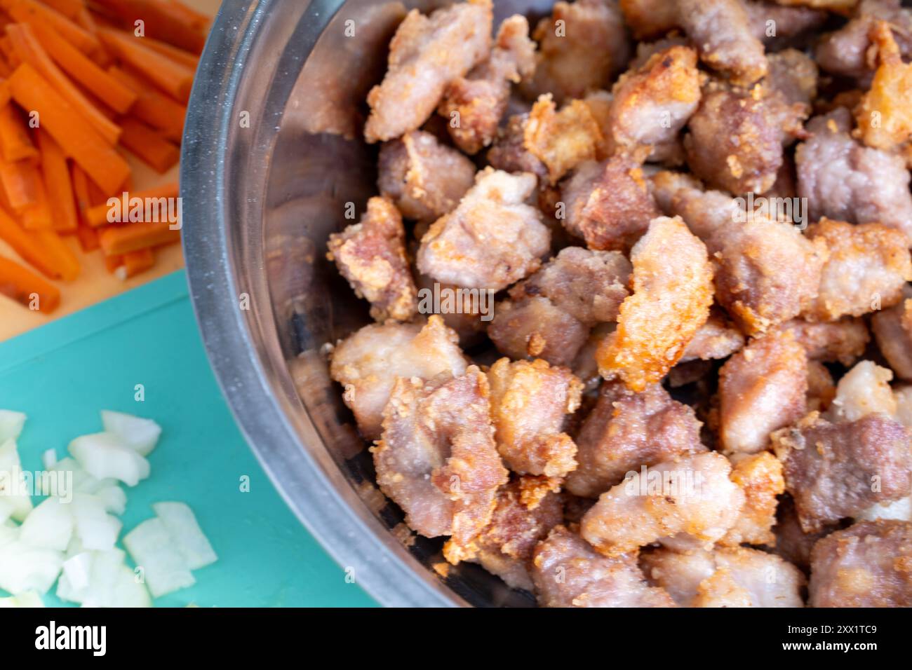 I pezzi di maiale tritati fritti in una ciotola accanto alle carote e alle cipolle vengono preparati per cuocere ulteriormente il maiale in una salsa dolce e acida secondo la Foto Stock