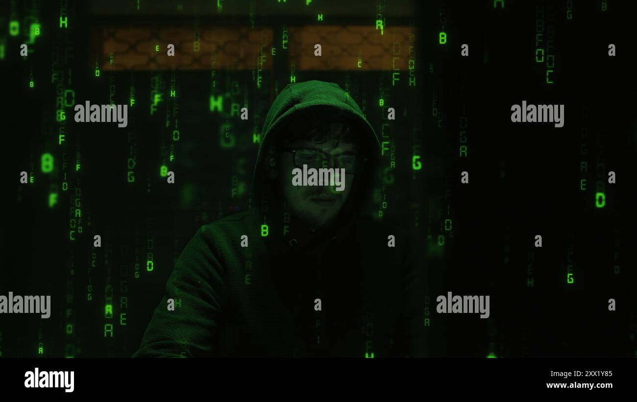 Un hacker incappucciato in una felpa con cappuccio scura siede in una stanza poco illuminata, circondato da un codice verde che si illumina a cascata sullo schermo. Il mondo segreto e oscuro Foto Stock