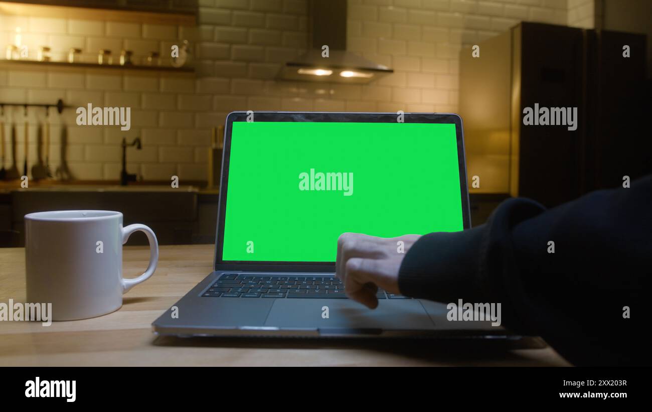 Un notebook con schermo verde su un piano di lavoro della cucina, tazza da caffè bianca. Una persona che utilizza un notebook nella cucina moderna. Adatto per aziende, tecnologia Foto Stock