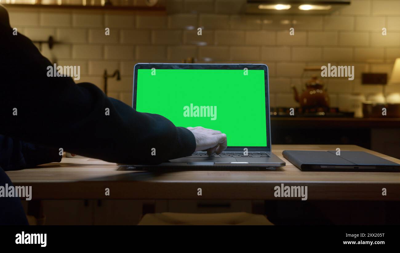 Un notebook con schermo verde su un piano di lavoro della cucina, tazza da caffè bianca. Una persona che utilizza un notebook nella cucina moderna. Foto Stock
