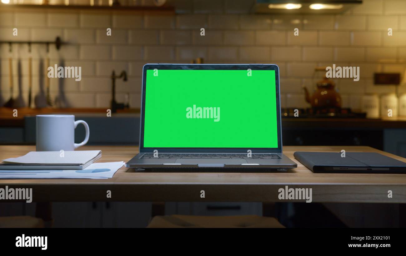 Un notebook con schermo verde con un tablet, una tazza di caffè e documenti su un tavolo di legno, sottolineando la produttività e l'organizzazione. Foto Stock