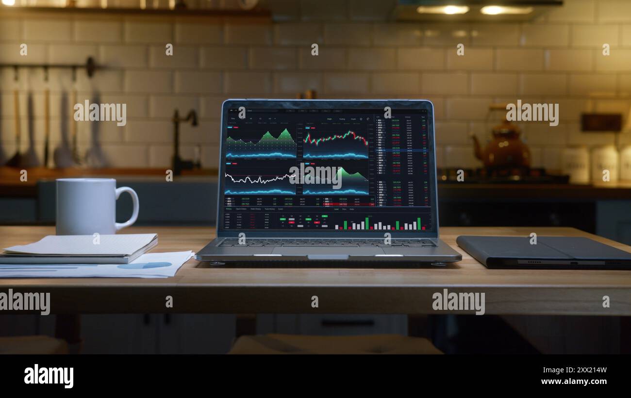 Un notebook che visualizza grafici finanziari e dati di borsa su un tavolo di legno in cucina. Commerciante a domicilio o analista, concetto finanziario Foto Stock