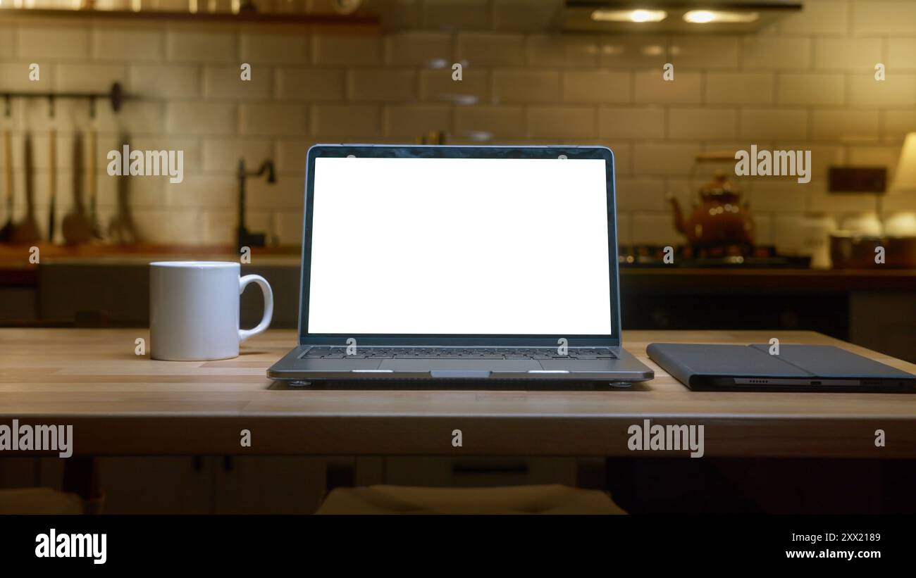 Un computer portatile con display cromatico a schermo bianco su un ripiano della cucina con una tazza da caffè bianca in una cucina moderna. Foto Stock
