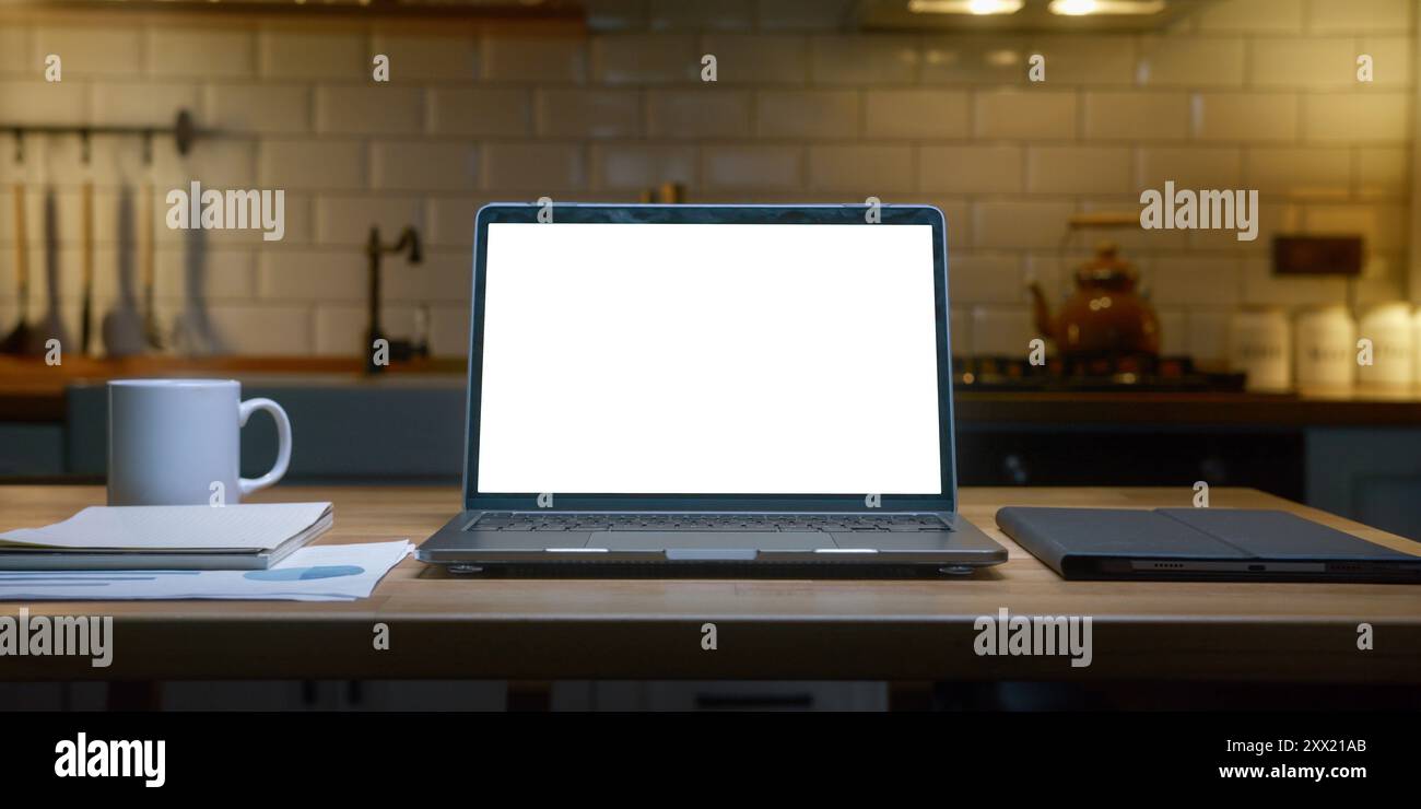 Computer portatile con display cromatico a schermo bianco su un ripiano della cucina con una tazza da caffè bianca in una cucina moderna. Foto Stock