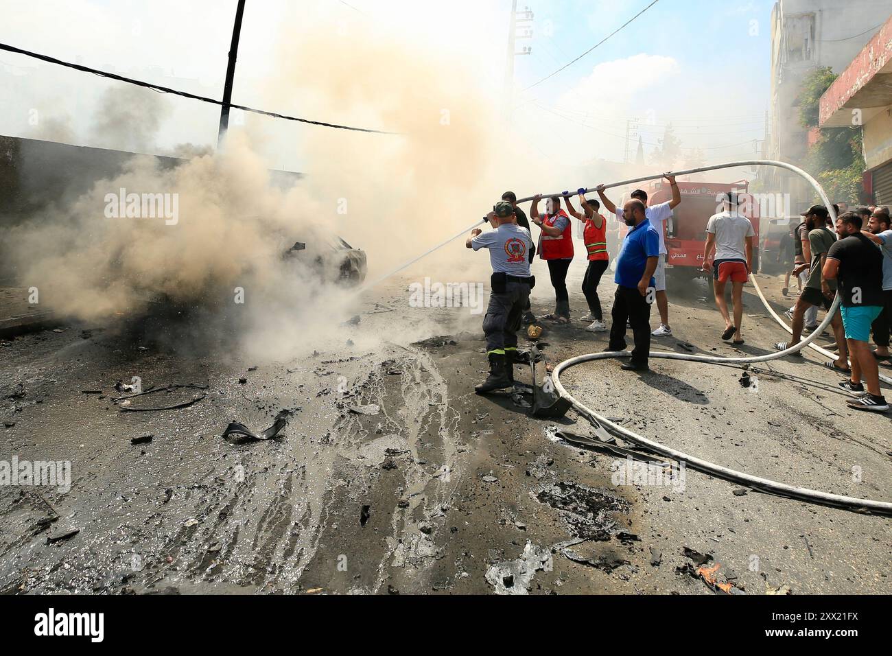 Sidon, Libano. 21 agosto 2024. La gente cerca di spegnere un incendio su un veicolo colpito da missili di un drone israeliano a Sidone, Libano, il 21 agosto 2024. Un drone israeliano ha sparato due missili aria-superficie su un SUV civile all'ingresso meridionale della città di Sidone mercoledì mattina, uccidendo un leader delle Brigate martiri di al-Aqsa, l'ala armata del movimento di Liberazione Nazionale palestinese (Fatah), hanno detto fonti militari libanesi a Xinhua. Crediti: Ali Hashisho/Xinhua/Alamy Live News Foto Stock