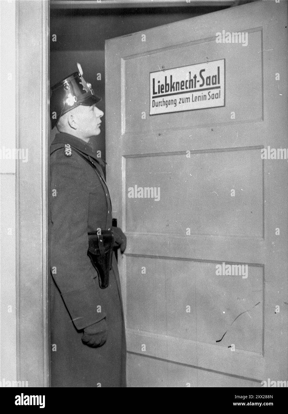 Un membro della Schutzpolizei si trova alla porta della Liebknecht Hall durante la chiusura della Karl-Liebknecht House, (sede del KPD) a Berlino. Dopo che a Hitler fu dato il potere, si mosse rapidamente ed efficacemente per mantenerlo. Dopo che il Reichstag fu bruciato, i comunisti furono incolpati (chi effettivamente appiccò il fuoco è ancora in dubbio). Dopo una frenetica campagna anticomunista furono dichiarati illegali, i membri furono imprigionati, i loro uffici saccheggiati e tutte le letterature distrutte. Con l'opposizione affettiva eliminata, i nazisti vinsero facilmente le elezioni generali un mese dopo. Foto Stock