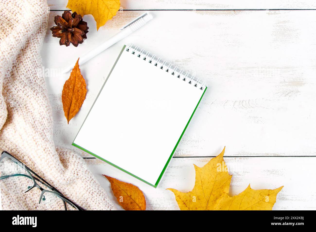 Ciao autunno. Foglie gialle, blocco note e bicchieri. Spazio di lavoro elegante. Composizione piatta su sfondo bianco di legno. Spazio di copia. Foto Stock