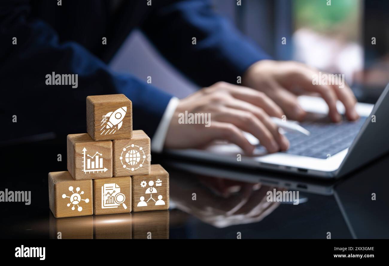 Un professionista lavora su un notebook, con blocchi di legno che rappresentano concetti aziendali chiave come marketing, lavoro di squadra e crescita. L'immagine mette in risalto il Foto Stock